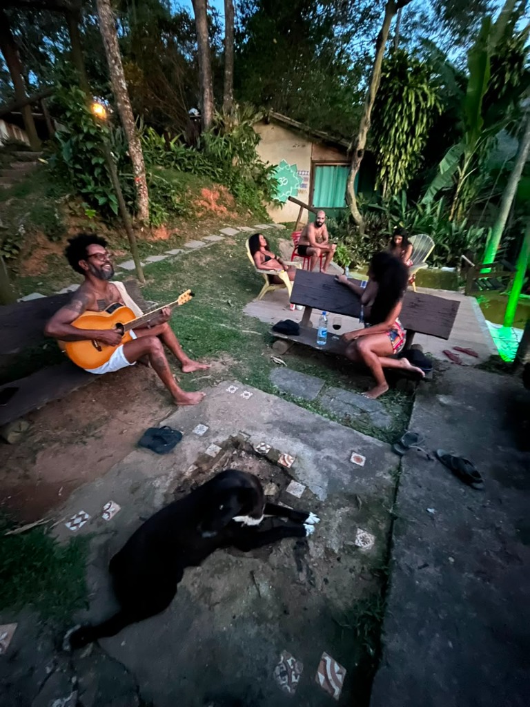 Roda de violão com amigos e cachorro no jardim ao entardecer